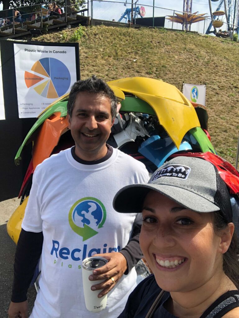 The photo shows two people standing outside in front of a pile of damaged car bumpers as part of the Reclaim Plastics display at the PNE.