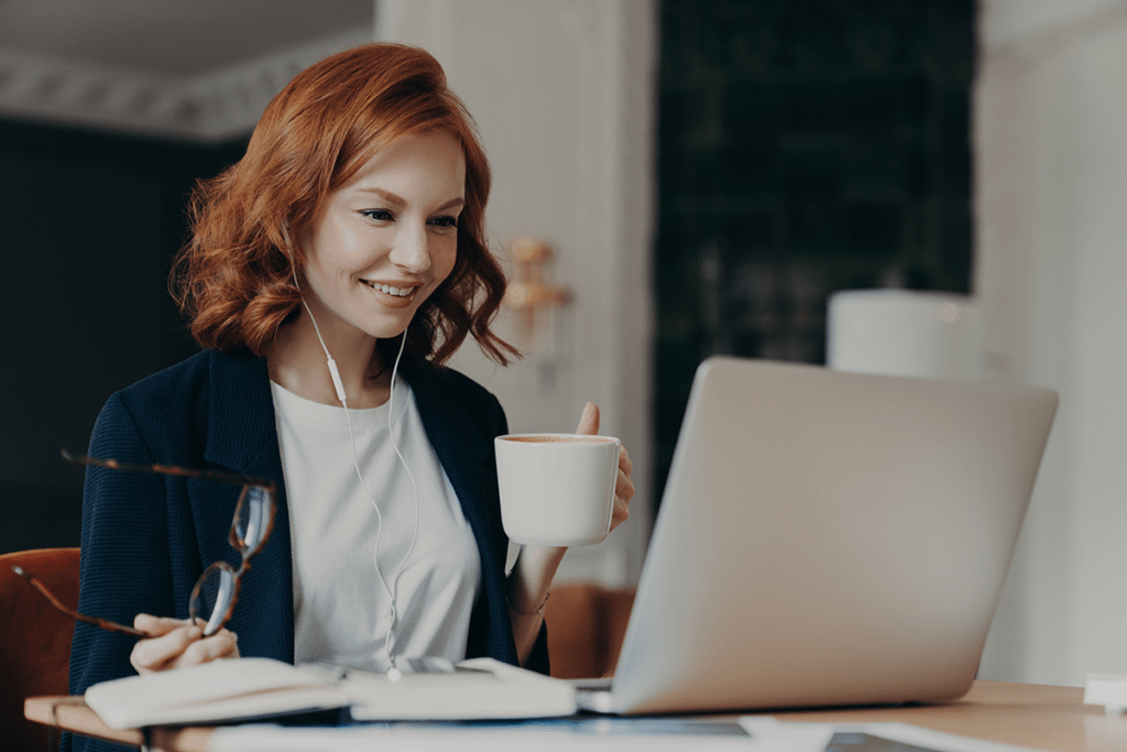 Young professional sits with her coffee, glasses, and laptop during a virtual event.