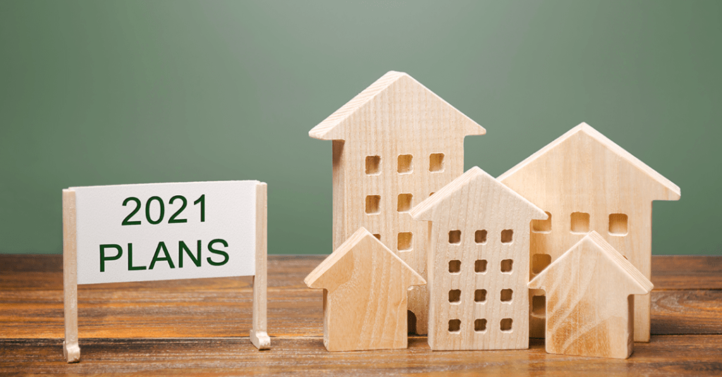 Photo of five wooden blocks shaped like homes and office buildings, with a sign that reads 2021 plans next to them.